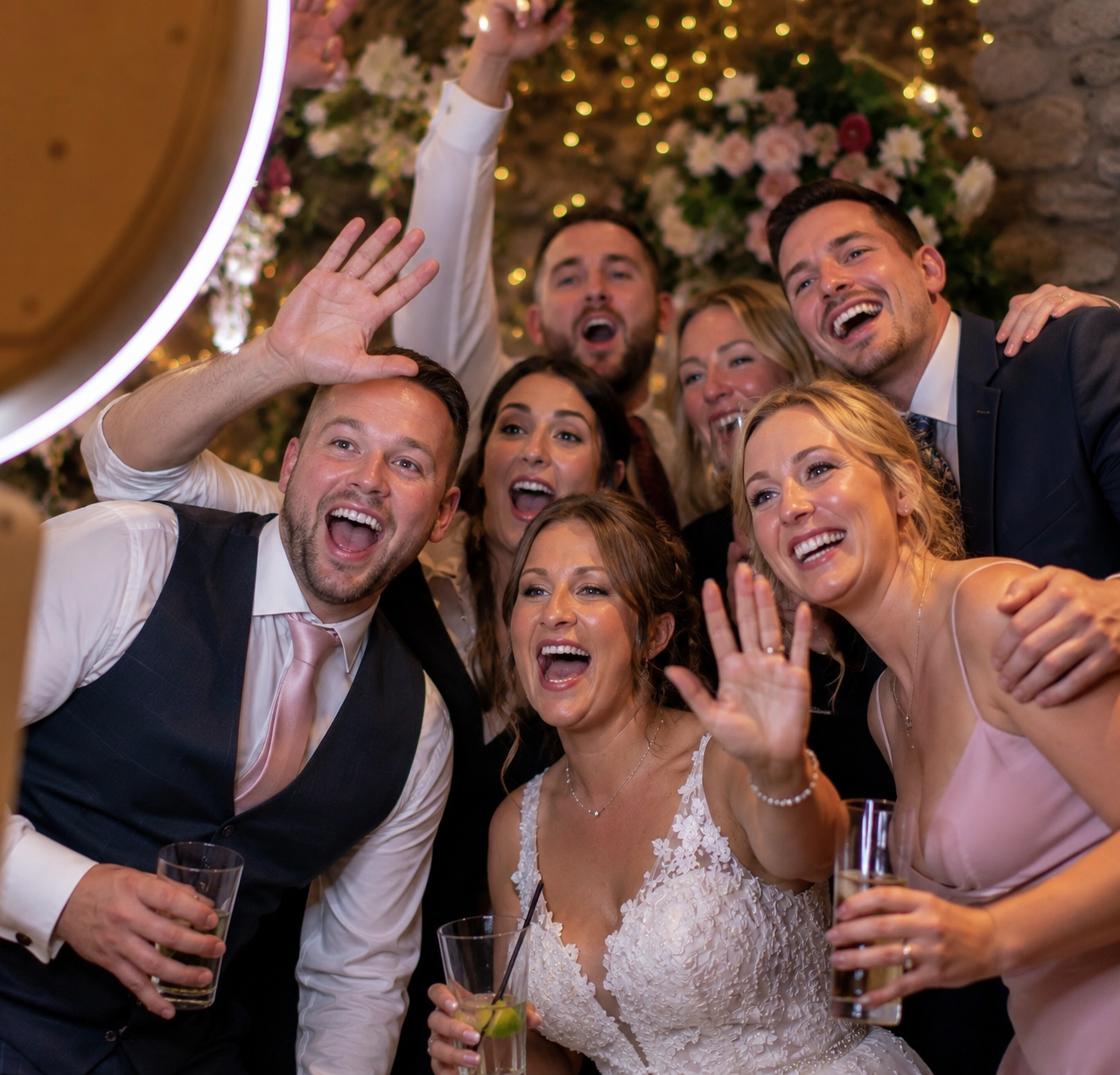 Wedding guests cheering in front of a floral backdrop selfie booth